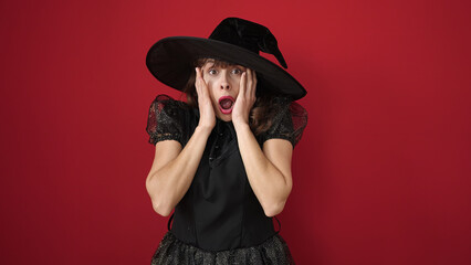 Poster - Young caucasian woman looking afraid with hands on face wearing witch costume over isolated red background