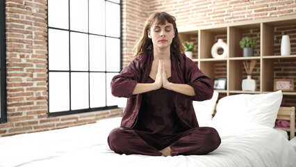 Poster - Young caucasian woman doing yoga posture sitting on bed at bedroom