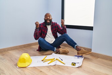 Sticker - African american man sitting on the floor at new home looking at blueprints celebrating surprised and amazed for success with arms raised and open eyes. winner concept.