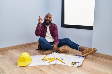 Sticker - African american man sitting on the floor at new home looking at blueprints pointing finger up with successful idea. exited and happy. number one.