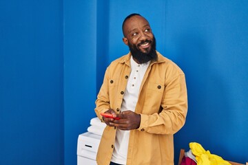 Sticker - Young african american man using smartphone waiting for washing machine at laundry room