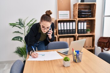 Wall Mural - Young woman business worker writing on document talking on smartphone at office