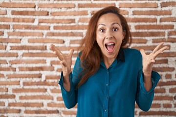 Sticker - Brunette woman standing over bricks wall celebrating crazy and amazed for success with arms raised and open eyes screaming excited. winner concept