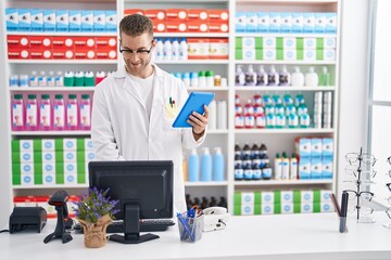 Wall Mural - Young caucasian man pharmacist using touchpad and computer at pharmacy