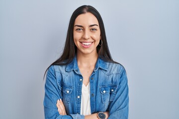 Canvas Print - Hispanic woman standing over blue background happy face smiling with crossed arms looking at the camera. positive person.