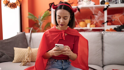 Poster - Young beautiful hispanic woman wearing devil costume using smartphone at home