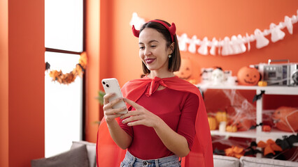 Sticker - Young beautiful hispanic woman wearing devil costume using smartphone at home