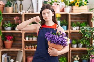 Canvas Print - Young caucasian woman working at florist shop holding pot with flowers with angry face, negative sign showing dislike with thumbs down, rejection concept