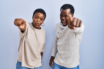 Canvas Print - Young african american couple standing over blue background together pointing displeased and frustrated to the camera, angry and furious with you