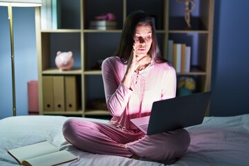 Canvas Print - Young hispanic woman using computer laptop on the bed hand on mouth telling secret rumor, whispering malicious talk conversation