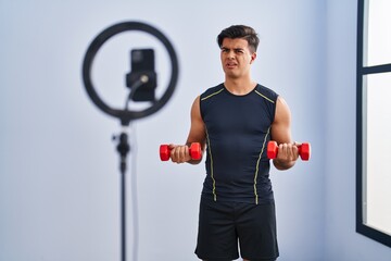 Poster - Hispanic man recording training tutorial at the gym clueless and confused expression. doubt concept.