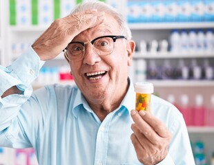 Wall Mural - Senior man with grey hair holding pills at the pharmacy stressed and frustrated with hand on head, surprised and angry face