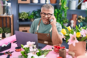 Poster - Middle age grey-haired man florist talking on smartphone using laptop at flower shop