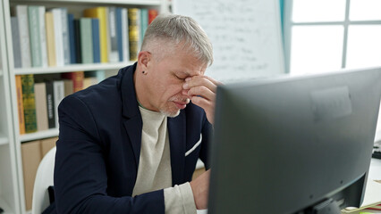 Middle age grey-haired man teacher using computer stressed at university classroom