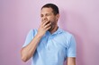 Hispanic man standing over pink background bored yawning tired covering mouth with hand. restless and sleepiness.