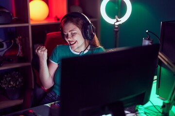 Poster - Redhead woman playing video games very happy and excited doing winner gesture with arms raised, smiling and screaming for success. celebration concept.