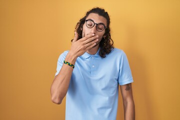 Poster - Young hispanic man standing over yellow background bored yawning tired covering mouth with hand. restless and sleepiness.