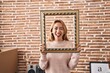 Hispanic woman holding empty frame sticking tongue out happy with funny expression.