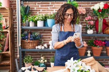 Sticker - Middle age woman florist smiling confident using smartphone at flower shop