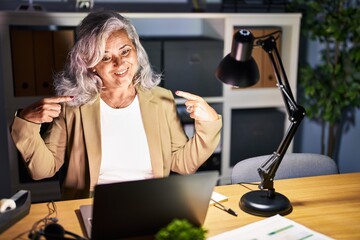 Sticker - Middle age woman with grey hair working using computer laptop late at night looking confident with smile on face, pointing oneself with fingers proud and happy.