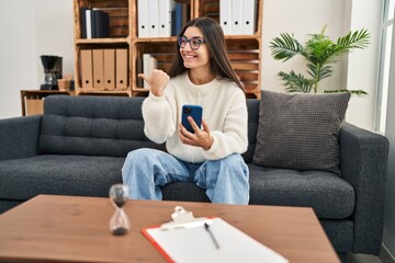 Canvas Print - Young hispanic woman going to therapy at consultation office pointing thumb up to the side smiling happy with open mouth