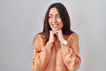 Sticker - Young brunette woman standing over white background laughing nervous and excited with hands on chin looking to the side