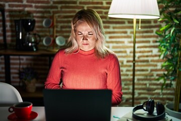 Wall Mural - Blonde woman using laptop at night at home with hand on stomach because nausea, painful disease feeling unwell. ache concept.