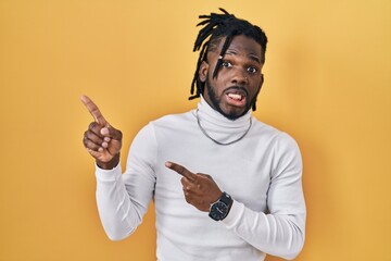 Wall Mural - African man with dreadlocks wearing turtleneck sweater over yellow background pointing aside worried and nervous with both hands, concerned and surprised expression