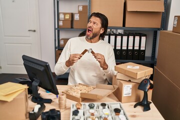 Canvas Print - Handsome middle age man working at small business ecommerce repairing watches angry and mad screaming frustrated and furious, shouting with anger. rage and aggressive concept.