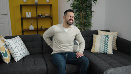 Sticker - Young hispanic man suffering for backache sitting on sofa at home