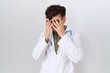 © Krakenimages.com - Young non binary man wearing doctor uniform and stethoscope with sad expression covering face with hands while crying. depression concept.