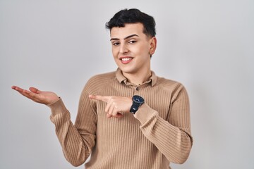 Poster - Non binary person standing over isolated background amazed and smiling to the camera while presenting with hand and pointing with finger.