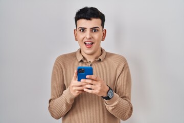 Poster - Non binary person using smartphone typing message celebrating crazy and amazed for success with open eyes screaming excited.