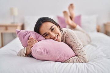 Poster - Young hispanic woman hugging pillow lying on bed at bedroom