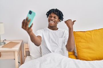 Canvas Print - Young african man with dreadlocks taking a selfie on the bed pointing thumb up to the side smiling happy with open mouth