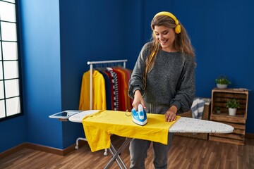 Wall Mural - Young blonde woman listening to music ironing clothes at laundry room