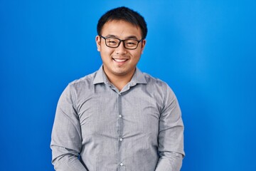 Poster - Young chinese man standing over blue background with a happy and cool smile on face. lucky person.