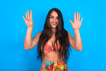 Poster - beautiful brunette woman wearing swimwear over blue background showing and pointing up with fingers number nine while smiling confident and happy.