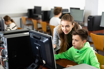 Wall Mural - Positive female teacher helping focused preteen schoolboy studying in college library computer lab..