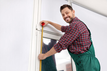 Canvas Print - Worker in uniform using tape measure while installing roller window blind indoors