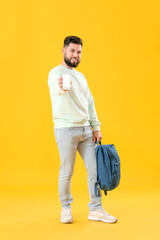 Canvas Print - Young bearded man with backpack and mobile phone on yellow background