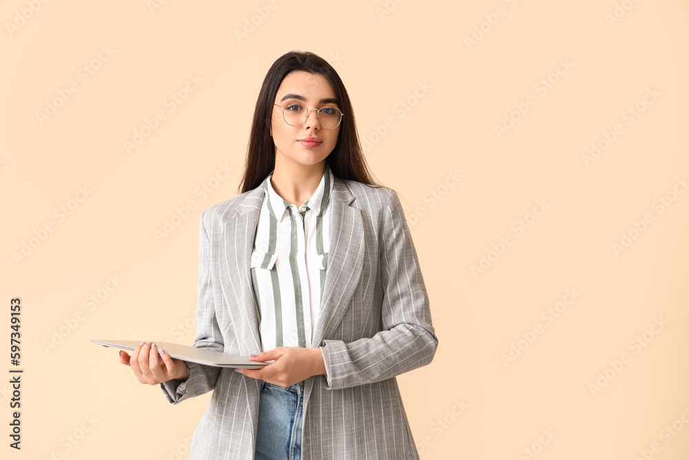 Young female programmer with laptop on beige background