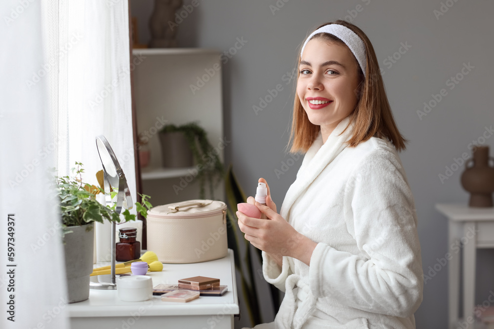 Young woman applying makeup foundation onto sponge at home
