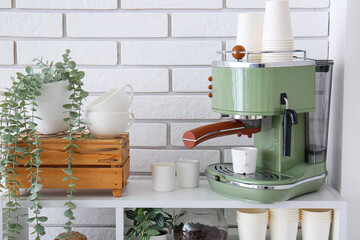 Modern coffee machine with cups and houseplants on shelving unit near white brick wall