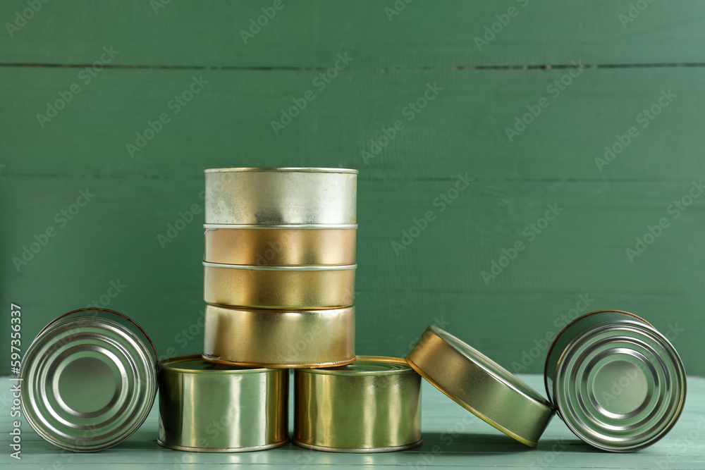 Different tin cans with fish on green wooden table