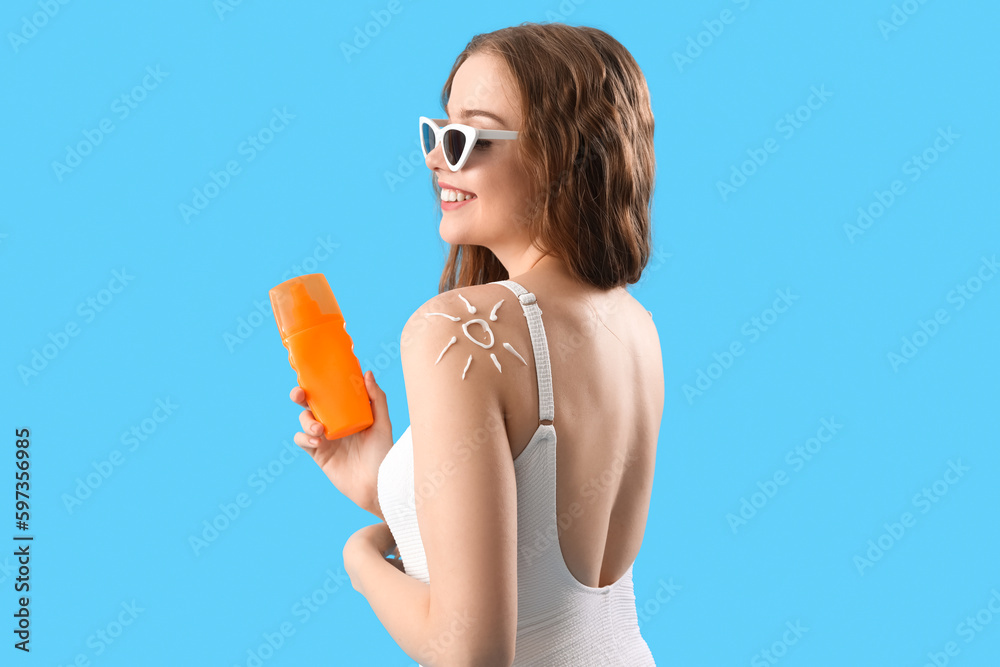 Beautiful young woman with sunscreen cream on blue background
