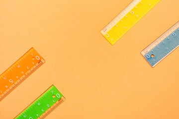 Colorful plastic rulers on orange background