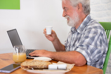 Sticker - Bearded senior caucasian man sitting at the table in coffee shop using laptop holding an espresso coffee cup. Elderly man at breakfast time while typing on computer