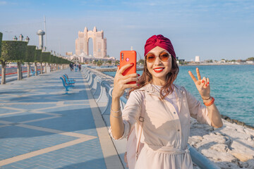 Wall Mural - Embodying the spirit of modernity and progress in the UAE's capital city, a girl snaps a photo against the dazzling skyline of Abu Dhabi