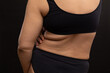 © Юля Бурмистрова - Female back in black underwear closeup. Plump woman touch fat folds on belly. Flaunt figure imperfections. Studio portrait over black background. Concept of obesity, body positive, self acceptance.